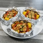 Foil Pack Meals with chicken potatoes corn and vegetables in opened foil packets