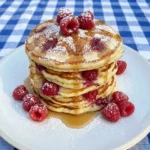 Stack of fluffy Lemon Raspberry Ricotta Pancakes with fresh raspberries and syrup