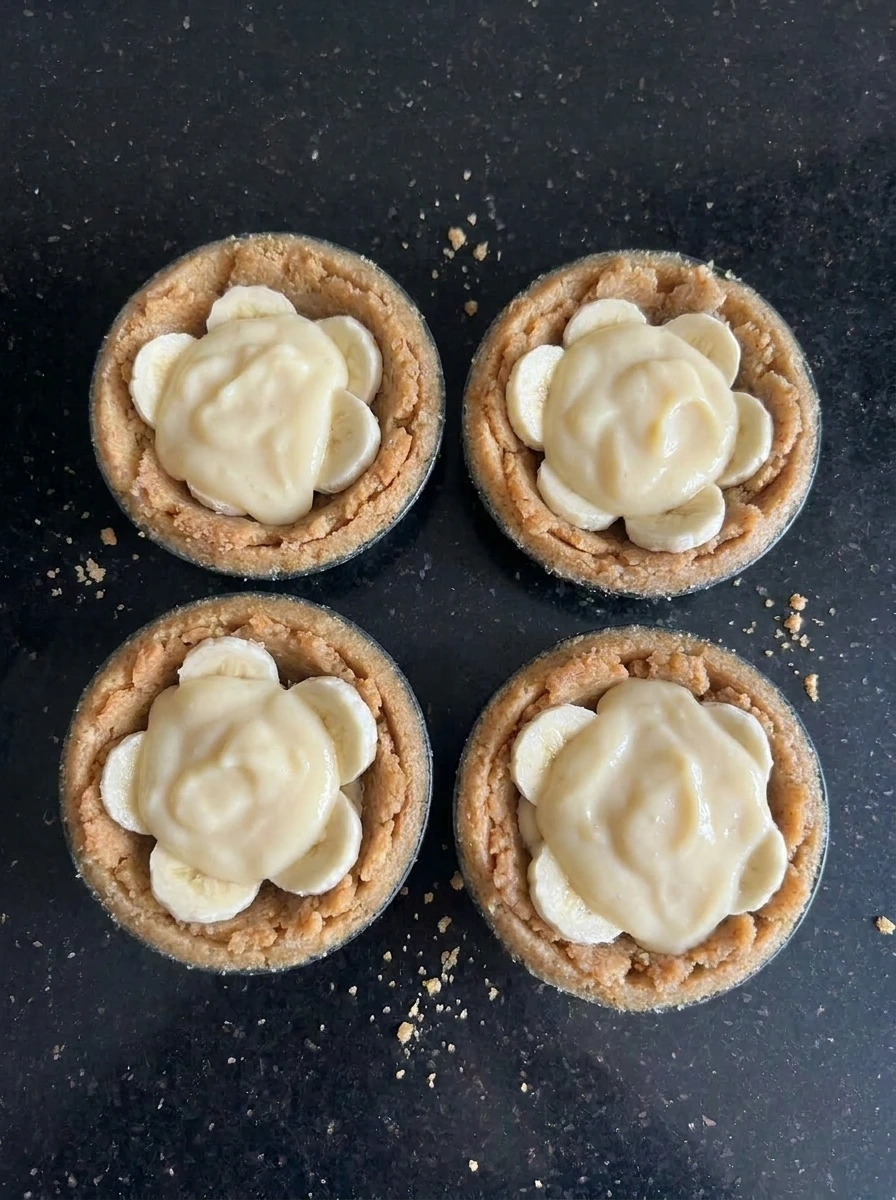Banana slices layered with pudding inside mini pie crusts.