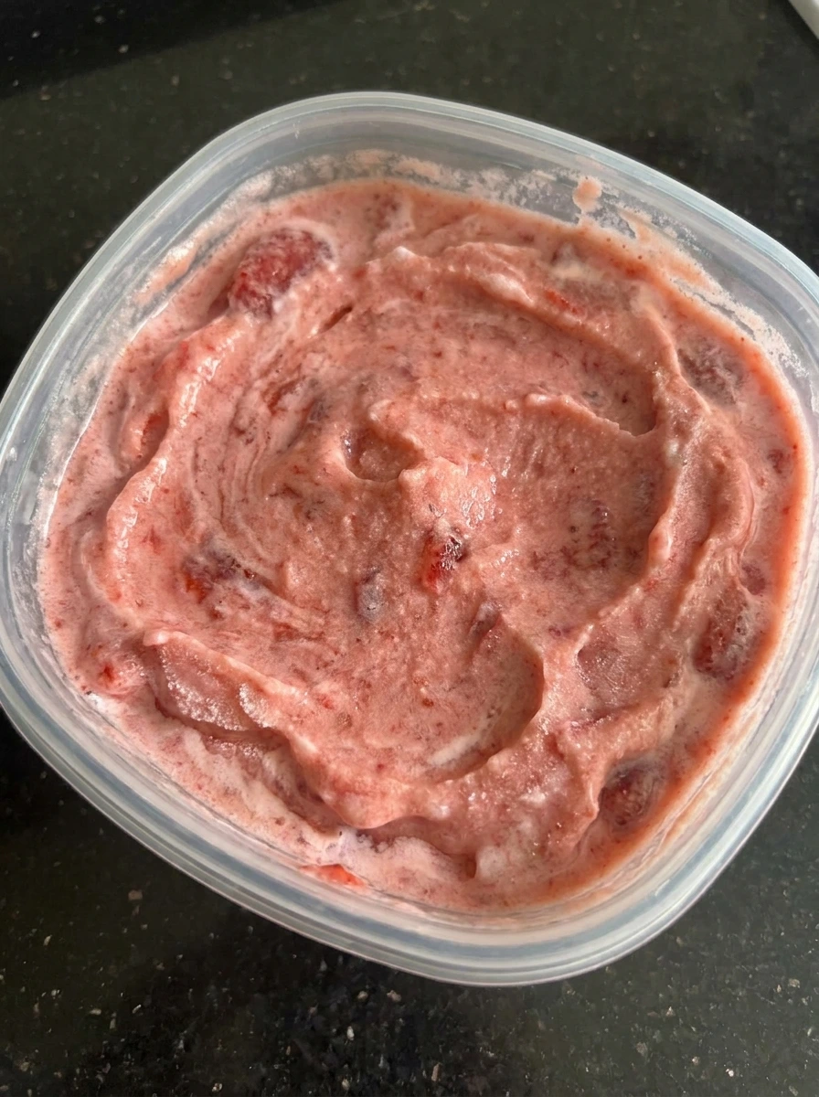 Partially frozen strawberry ice cream base with berry pieces.