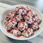 Strawberry Puppy Chow in a serving bowl with pink coating and powdered sugar