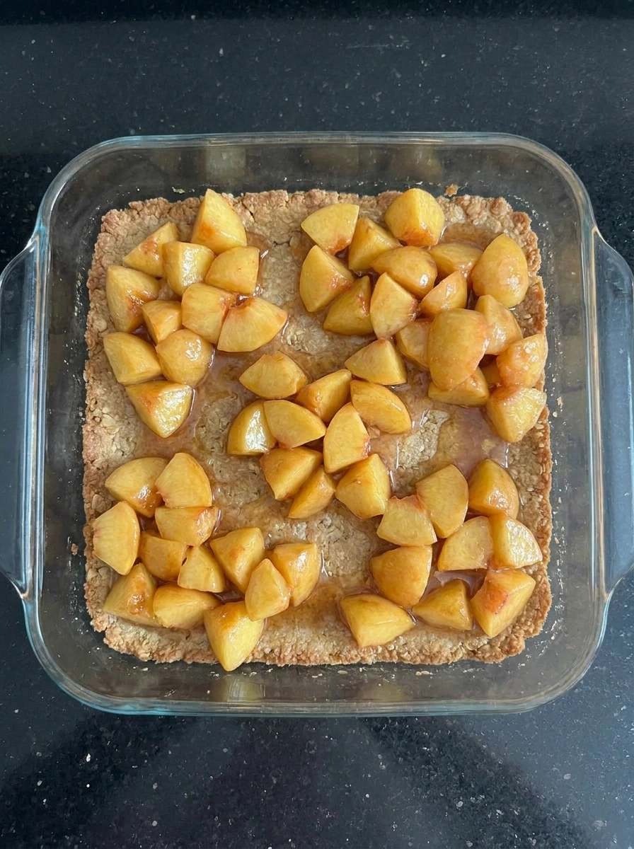 Peach filling layered over crust for Peach Crumble Bars Everyone Loves