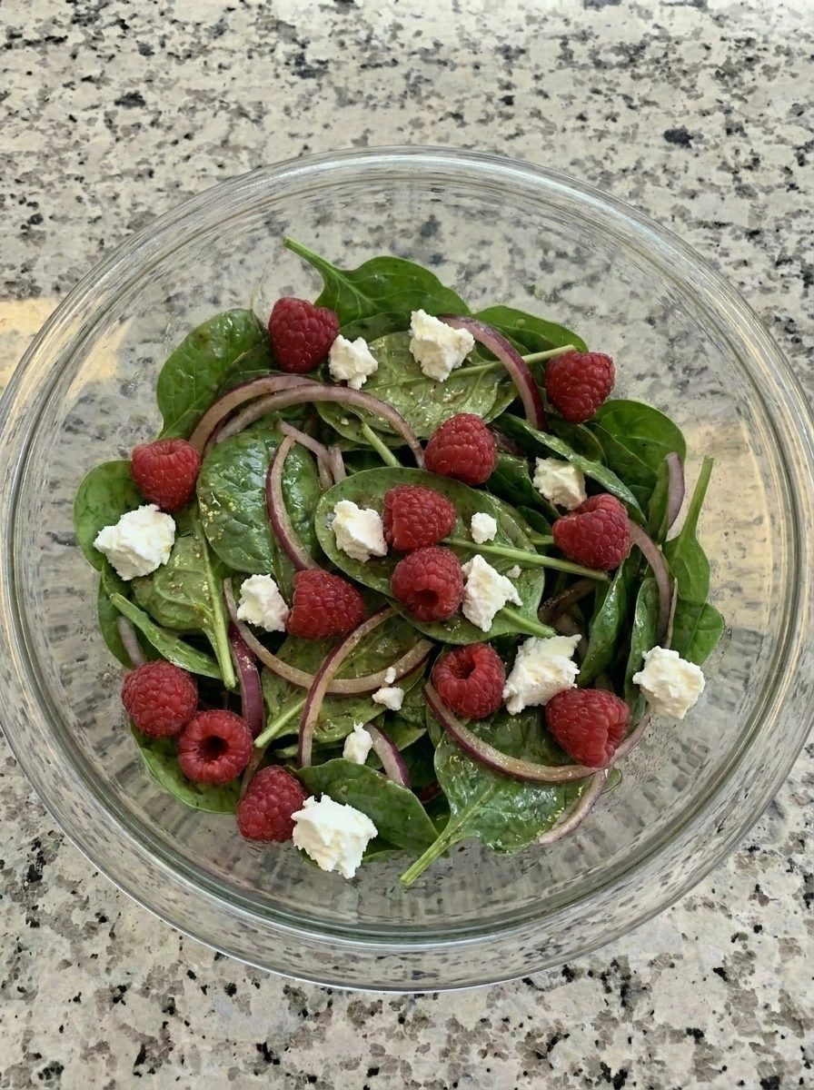 Raspberries and goat cheese scattered over spinach salad